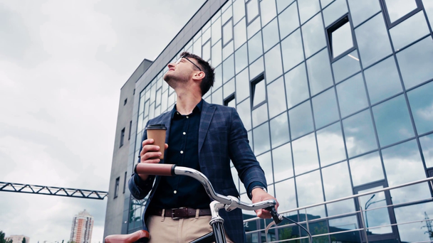cheerful man holding paper cup and standing near bike outside  - Filmagem, Vídeo
