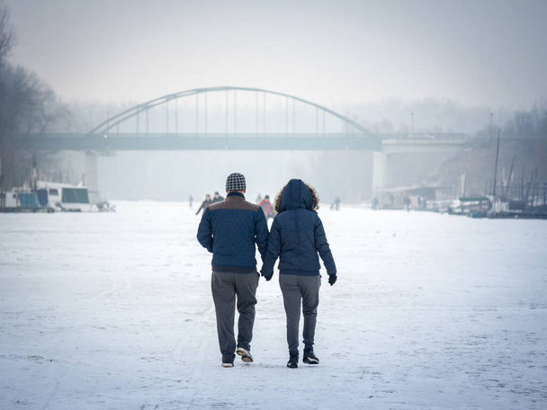 PANCEVO, SERBIA - JANUARY 22, 2017: People, a couple, walking on the frozen Timis Tamis river during the 2017 winter, in Pancevo. This winter was particularly harsh, paralyzing the activity on the rivers - Foto, Imagem