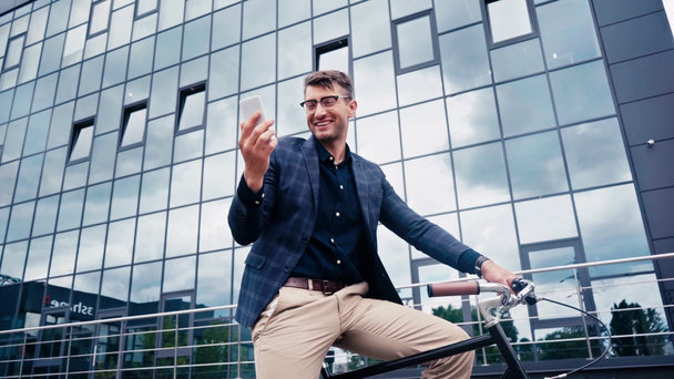 glücklicher Mann winkt Hand, während er Videoanruf in der Nähe von Gebäude und Fahrrad hat - Filmmaterial, Video