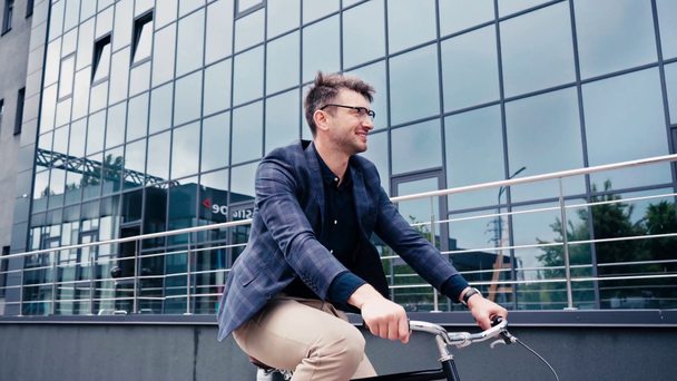 boldog férfi szemüvegben biciklizés az épület közelében  - Felvétel, videó