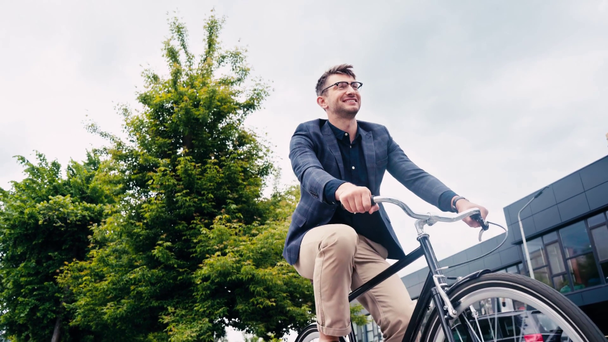 low angle view of happy man in glasses riding bicycle  - Felvétel, videó