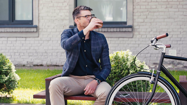 hombre feliz bebiendo café para ir y sentado en el banco cerca de la bicicleta
  - Imágenes, Vídeo