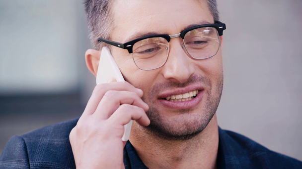 zbliżenie człowieka w okularach uśmiecha się podczas rozmowy na smartfonie - Materiał filmowy, wideo