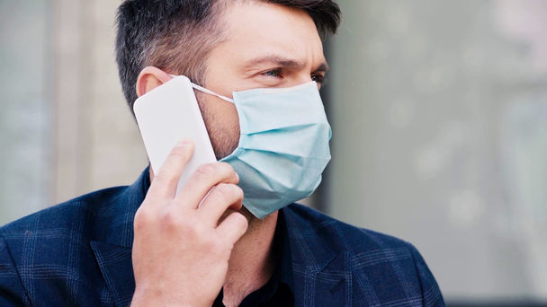 άνδρας με ιατρική μάσκα μιλάει στο smartphone έξω - Πλάνα, βίντεο