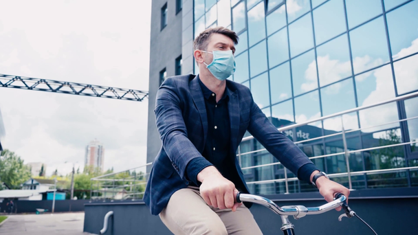 zakenman in medisch masker paardrijden fiets in de buurt van gebouw  - Video