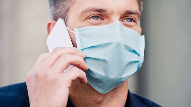 primo piano di uomo in maschera medica parlare su smartphone al di fuori - Filmati, video