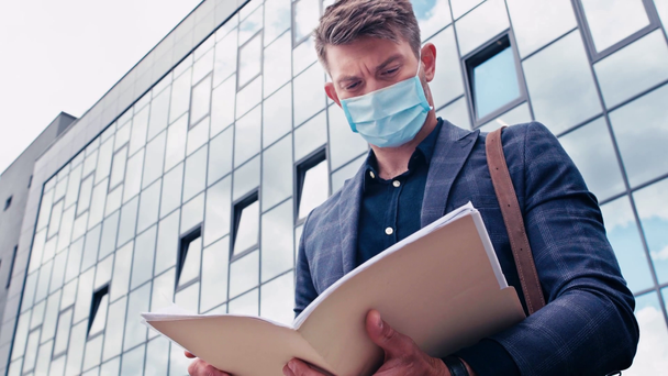 建物の近くの文書を見る医療用マスクの男性の低角度ビュー - 映像、動画