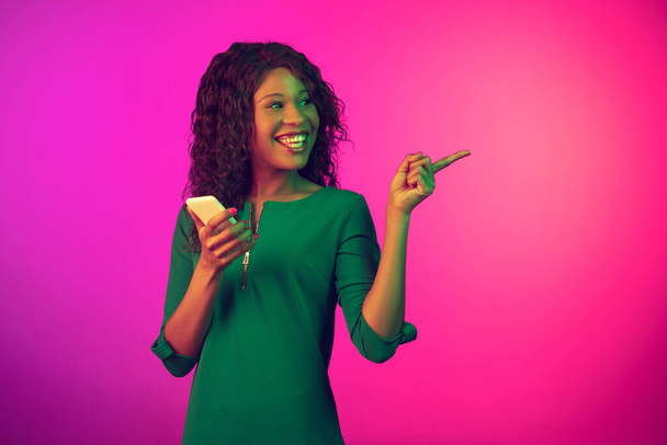 African-american young womans portrait isolated on gradient pink background in neon light - Photo, image