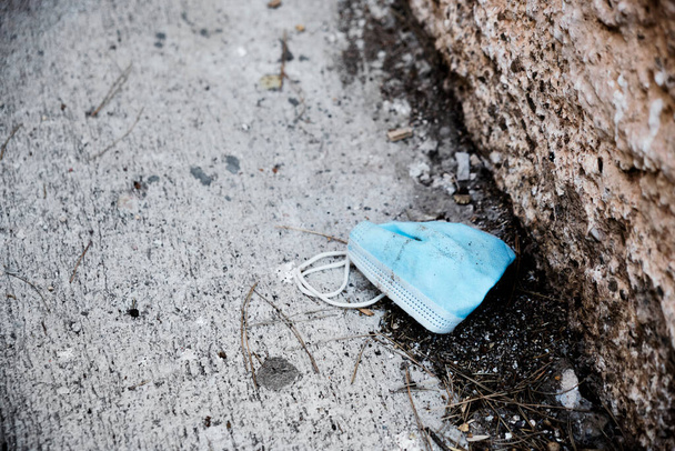Kullanılmış mavi cerrahi maskenin yakın plan fotoğrafı. Kaldırımın yanındaki kirli asfalta atılmış. - Fotoğraf, Görsel