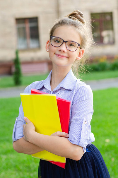 Back to school. Education concept. Cute smiling schoolgirl on the way to the school. Happy little girl child in glasses holding the books  - Photo, Image