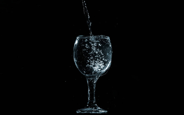 Gießen Sie Wasser in Glas auf schwarzem Hintergrund. - Foto, Bild