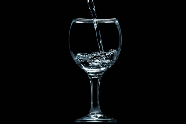 Ρίξτε νερό σε γυαλί σε μαύρο φόντο. - Φωτογραφία, εικόνα