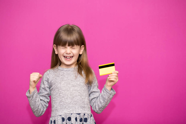 mooi jong meisje kid holding credit card zeer gelukkig en opgewonden, winnaar uitdrukking vieren overwinning schreeuwen met grote glimlach geïsoleerd op roze achtergrond - Foto, afbeelding