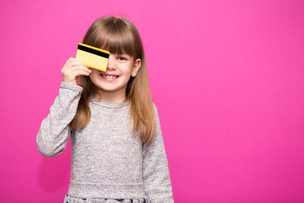 Šťastná holčička s kreditní kartou izolované na růžovém pozadí. - Fotografie, Obrázek
