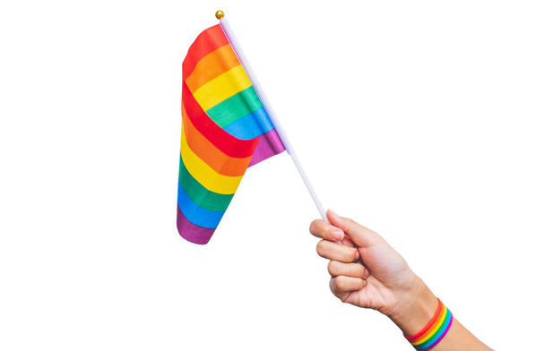  ręka z tęczowym paskiem na nadgarstku trzymającym tęczową flagę na białym tle. Gejowska kampania dumy. gej duma LGBT pojęcie - Zdjęcie, obraz