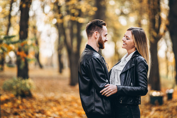 Beautiful young couple walking in the autumn park on a sunny day. They hug and smile, enjoy a walk. - Fotoğraf, Görsel