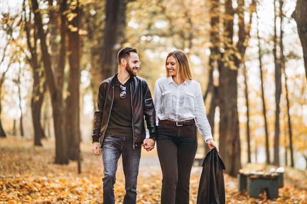 Portrait of a happy loving couple walking outdoor in the autumn park. Man and woman holding hands and smilling. - Φωτογραφία, εικόνα