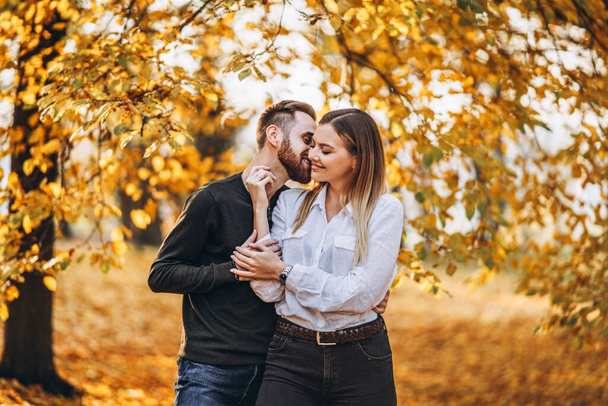 Sunny portrait of a young loving couple walking in the autumn park. They hug and smile, enjoy a walk. - Fotografie, Obrázek