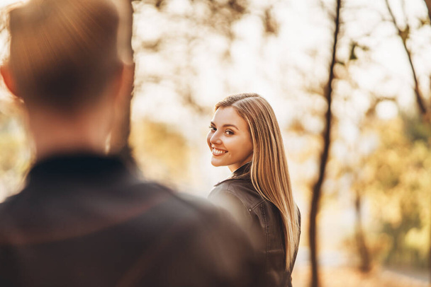 Retrato de uma jovem mulher sorridente no fundo do parque de outono. Em primeiro plano, uma silhueta turva de um homem
. - Foto, Imagem
