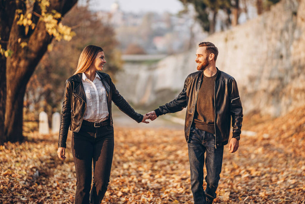 Full length portrait of a happy loving couple walking outdoor in the autumn park. Man and woman holding hands. - Фото, изображение