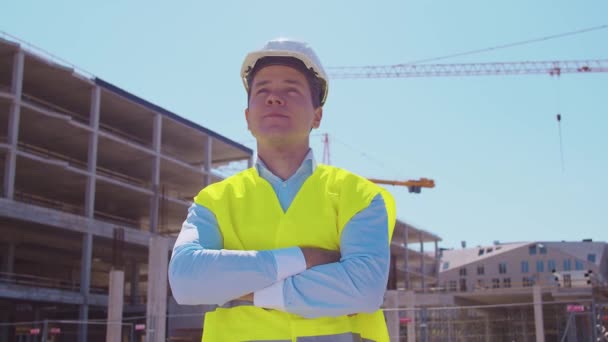 Professional builder standing in front of construction site. Foreman in hardhat helmet and vest. Office building and crane background. Business, real estate and investment concepts. - Footage, Video