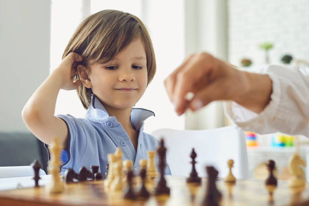 Adorable little boy playing chess with his mom at home. Cute child enjoying strategy board game with his parent indoors - Foto, Bild