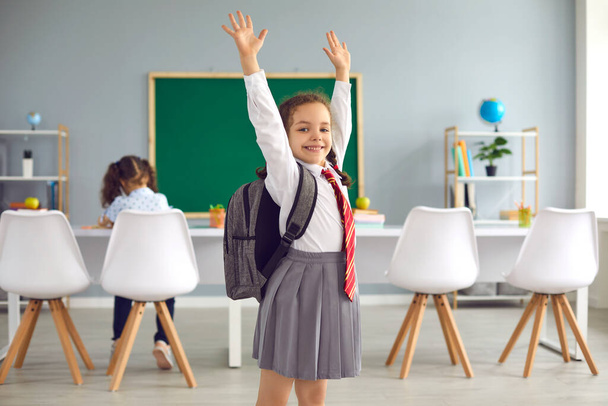 Concept back to school. Happy schoolgirl smiling raised her hands up while standing in class. - Фото, изображение