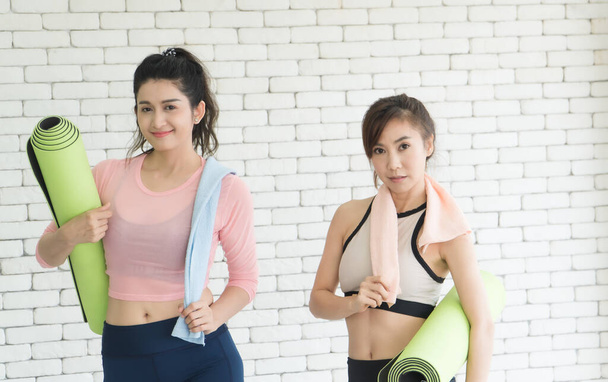 Portret pięknej, atrakcyjnej, zdrowej kobiety, dwóch Azjatów z matami ćwiczeniowymi rozmawiających na siłowni po jodze - Zdjęcie, obraz