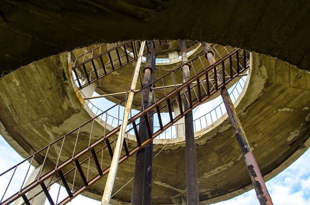 Abandoned pumping station. Water tower of concrete and wood, metal stairs and railings. Down the spiral staircase. Art curve stair with a few rainning. Selecive focus image. - Fotografie, Obrázek