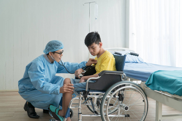 Médicos Voluntários Asiáticos Cuidando e Ajudando na Reabilitação de Meninos Deficientes Fique no hospital. O rapaz é aleijado, os asiáticos não conseguem evitar. Deve estar sentado numa cadeira de rodas o tempo todo.
 - Foto, Imagem