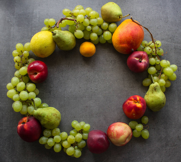 Summer fruit composition. Colorful grapes, nectarines, mango and pears wreath top view photo. Dark grey textured background with copy space.  - Фото, изображение