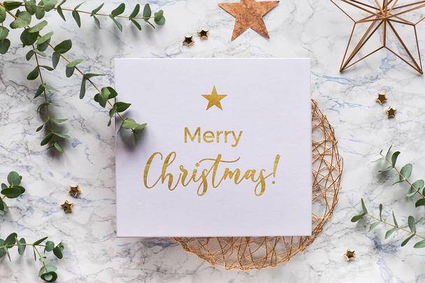 Christmas frame with fresh eucalyptus twigs and golden geometric decorations - hexagons, trinkets and wire shapes. Flat lay, top view on white marble background with text Merry Christmas in gold. - Photo, Image