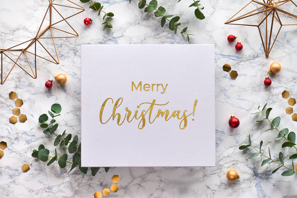 Light Christmas frame with fresh eucalyptus twigs and golden geometric decorations - hexagons, trinkets and wire shapes. Flat lay on white marble background with text Merry Christmas on canvas - Foto, imagen