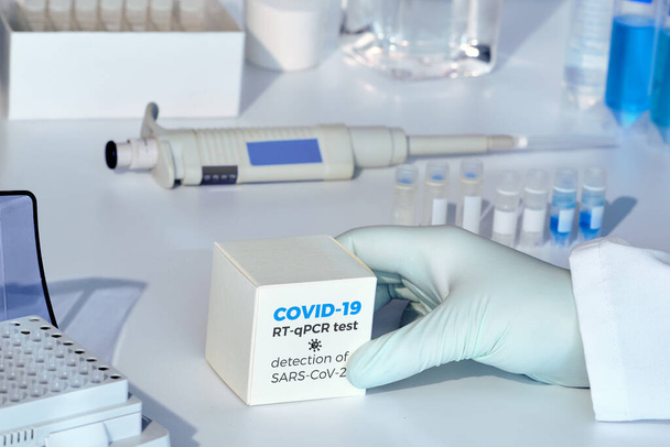 Quick novel COVID-19 coronavirus test kit. SARS-CoV-2 pcr diagnostics kit. Hand in glove with the box. The kit detects covid19 illness. - Fotó, kép