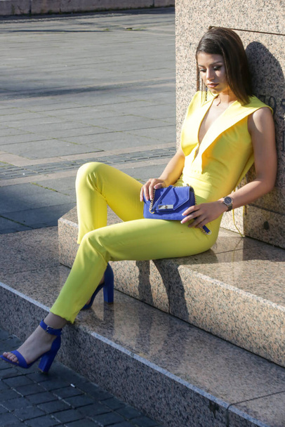 Portrait extérieur de jeune femme à la mode portant une combinaison jaune et des accessoires bleus - Photo, image
