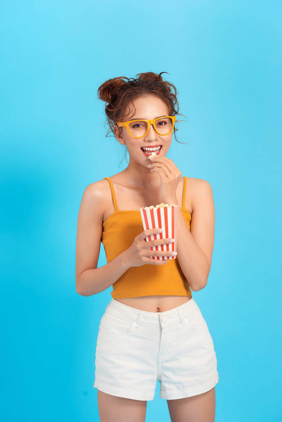 Красивая девушка ест попкорн и смотреть комедийный фильм изолированы на синем фоне
 - Фото, изображение