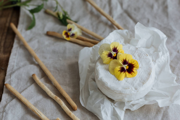 Camembert cheese head is decorated with flowers and is on a linen napkin. - Foto, immagini