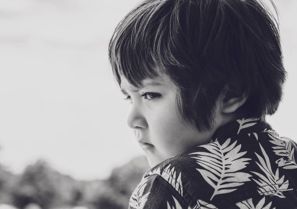 Küçük çocuğun duygusal portresi üzgün bir yüzle aşağıya bakıyor, yüzü sıkılmış bir çocuğun, güneşli bir günde parkta tek başına dikilirken görüntüsü.. - Fotoğraf, Görsel