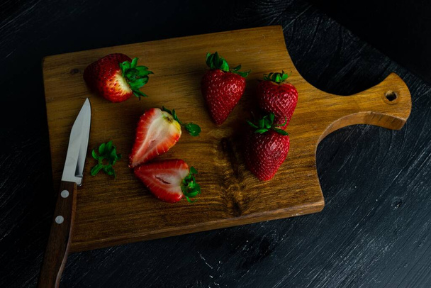 A top view of fresh ripe strawberries and a sharp knife on a wooden board - Foto, Imagem