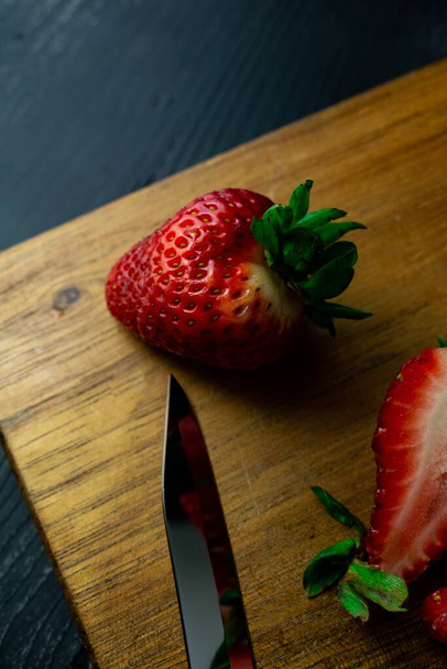 A vertical closeup shot of fresh ripe strawberries and a sharp knife on a wooden board - Foto, Imagen