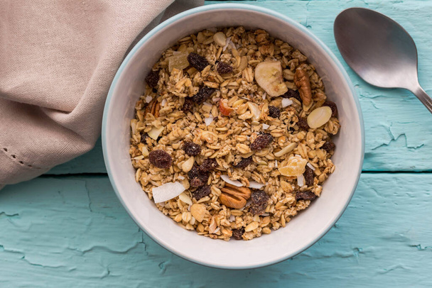 Granola in bowl with raisins,dried banana,  nuts - top view breakfast muesli on rustic blue table background - Photo, Image