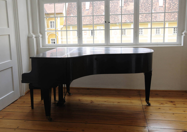 Bir pencerenin yanında duran piyano, telli bir müzik aleti. - Fotoğraf, Görsel