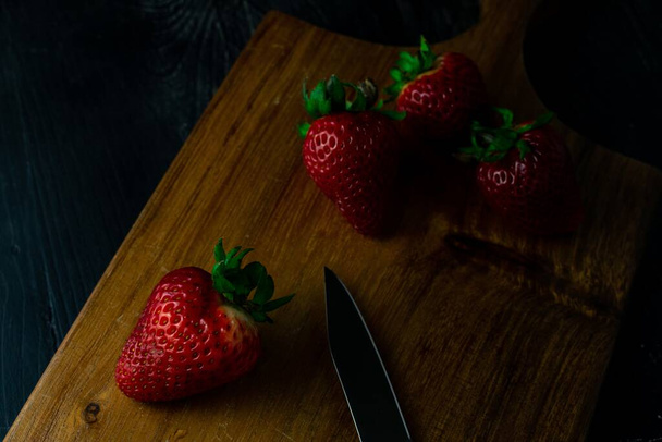 A closeup shot of fresh ripe strawberries and a knife on a wooden board - 写真・画像
