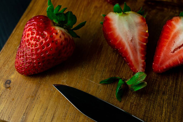 A top view of fresh ripe strawberries and a sharp knife on a wooden board - Foto, Imagen