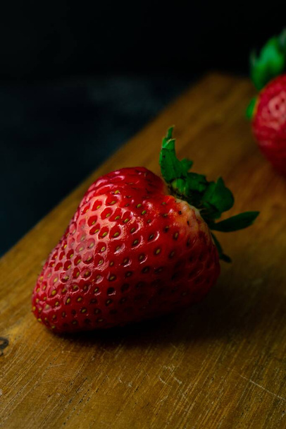 A vertical closeup shot of fresh ripe strawberries on a wooden board - Zdjęcie, obraz
