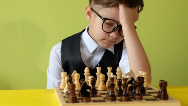 Kind spielt Schach am Tisch. Kleiner Junge mit Brille entwickelt Schachstrategie, spielt Brettspiel mit Freund. - Filmmaterial, Video