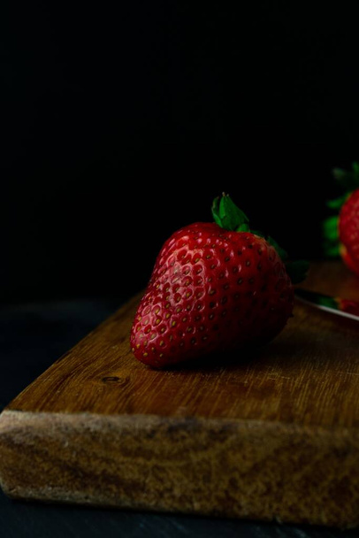 A vertical closeup shot of fresh ripe strawberries on a wooden board - 写真・画像
