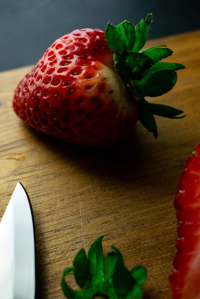 A vertical closeup shot of fresh ripe strawberries and a sharp knife on a wooden board - Foto, Imagen