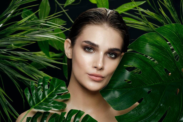 Femme confiante avec un maquillage lumineux près des feuilles vertes des palmiers  - Photo, image