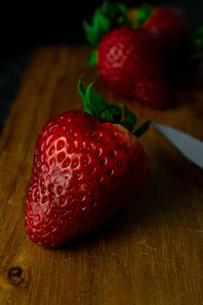 A vertical closeup shot of fresh ripe strawberries on a wooden board - Foto, Imagen
